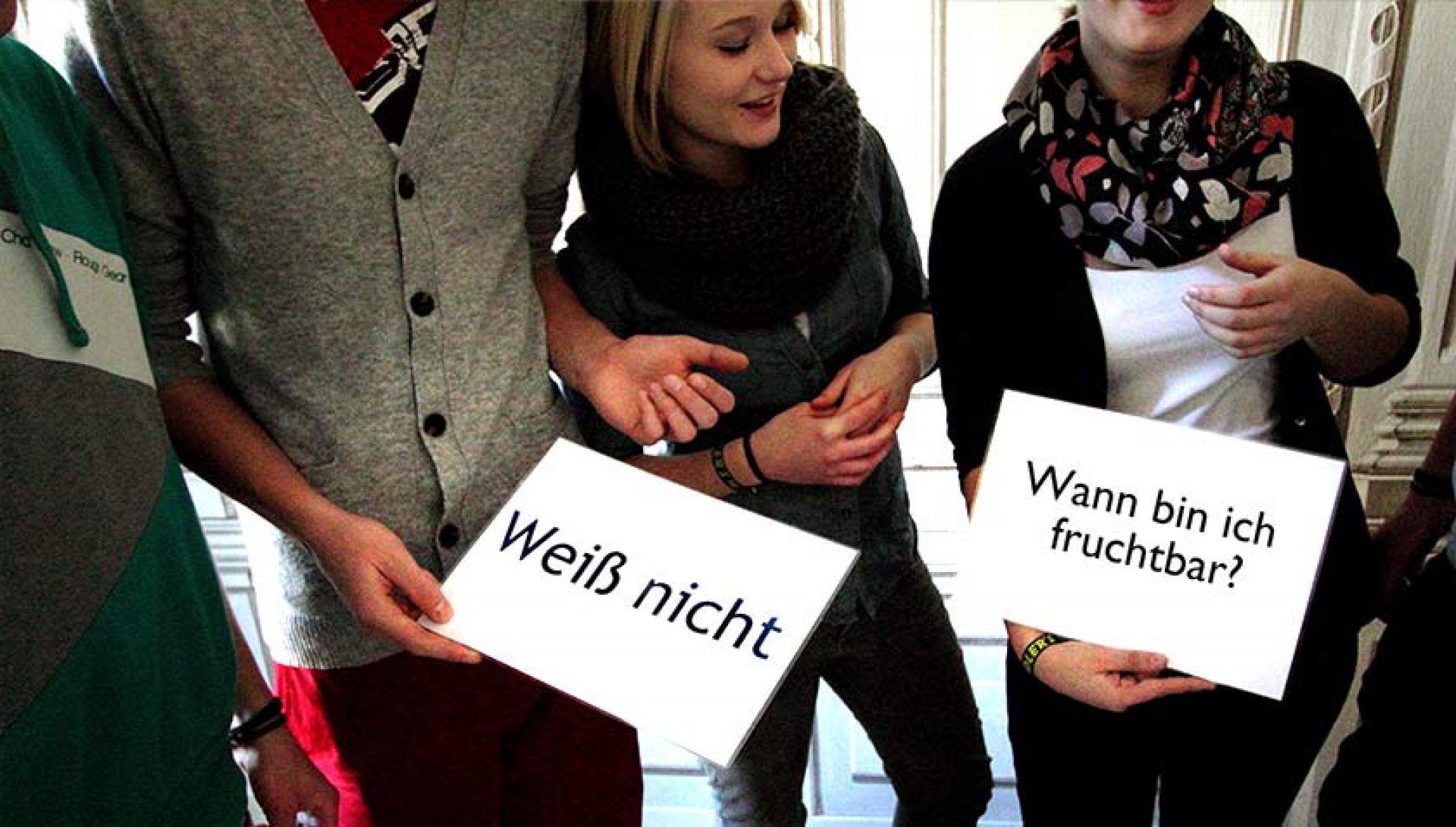 Teilnehmerinnen einer Fortbildung halten Karten mit „Weiß nicht“ und „Wann bin ich fruchtbar?“
