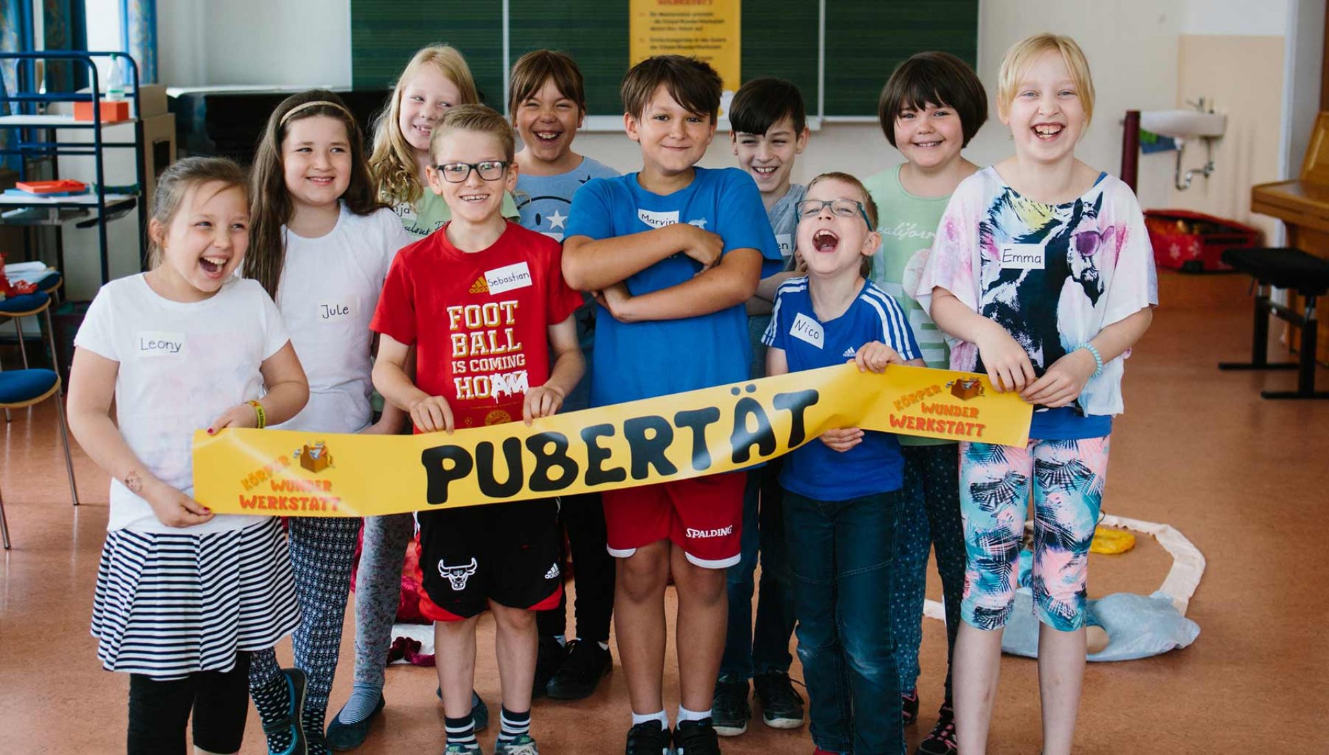 Kinder einer 4. Klasse halten gemeinsam ein Banner mit der Aufschrift „Pubertät“